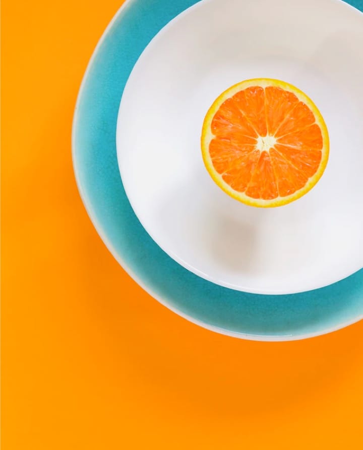 Image of an orange sliced through the center placed on a plate with an orange background