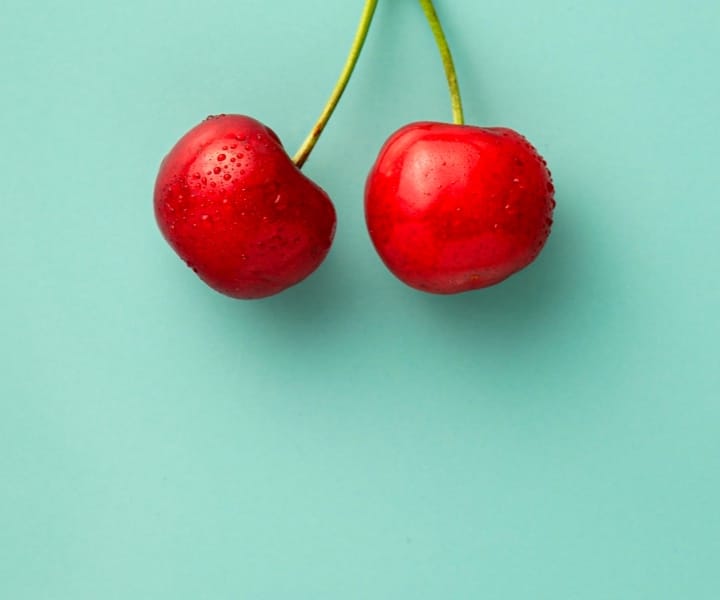 Image of two cherries hanging infront of a cyan background