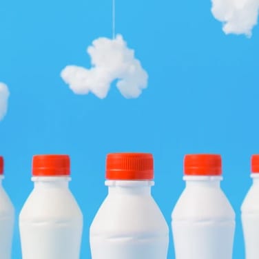 Image of milk bottles placed in front of a scene with fake clouds