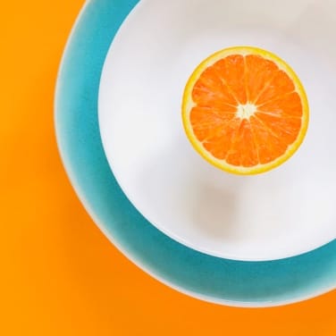 Image of an orange sliced through the center placed on a plate with an orange background